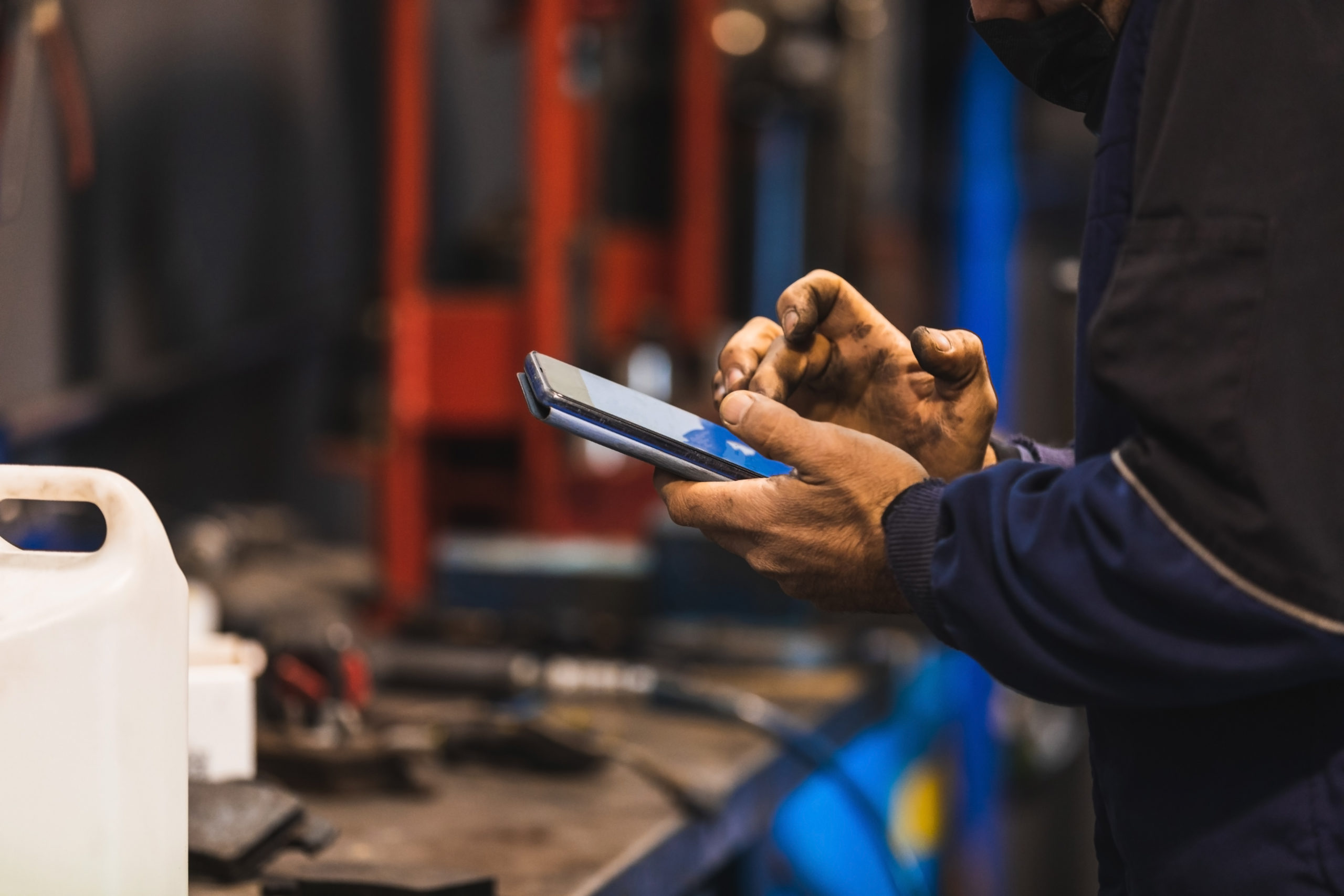 Mechanic using cell phone in the workshop. Hands full of grease.